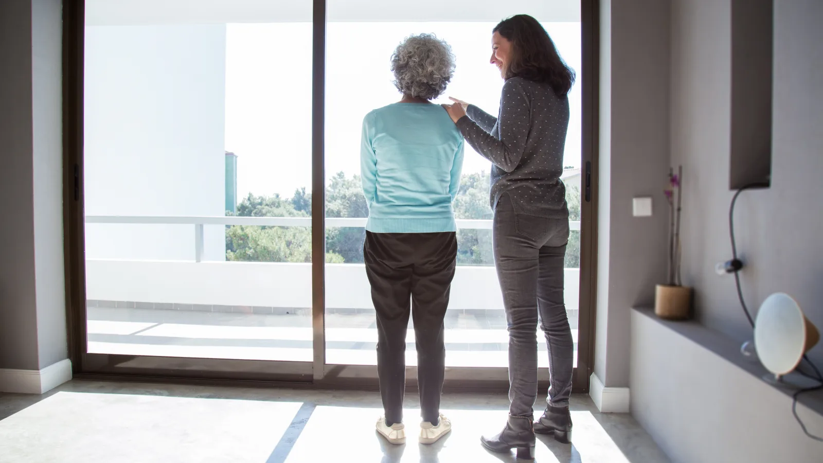 Fille adulte faisant visiter un logement lumineux et spacieux à sa mère âgée souriante