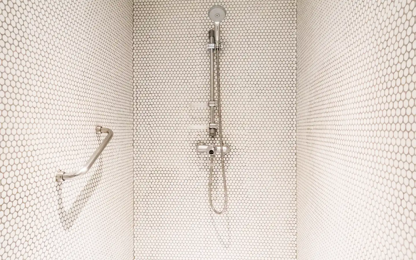 Une douche de plain-pied carrelée est équipée d’une barre d’appui et d’une douchette réglable