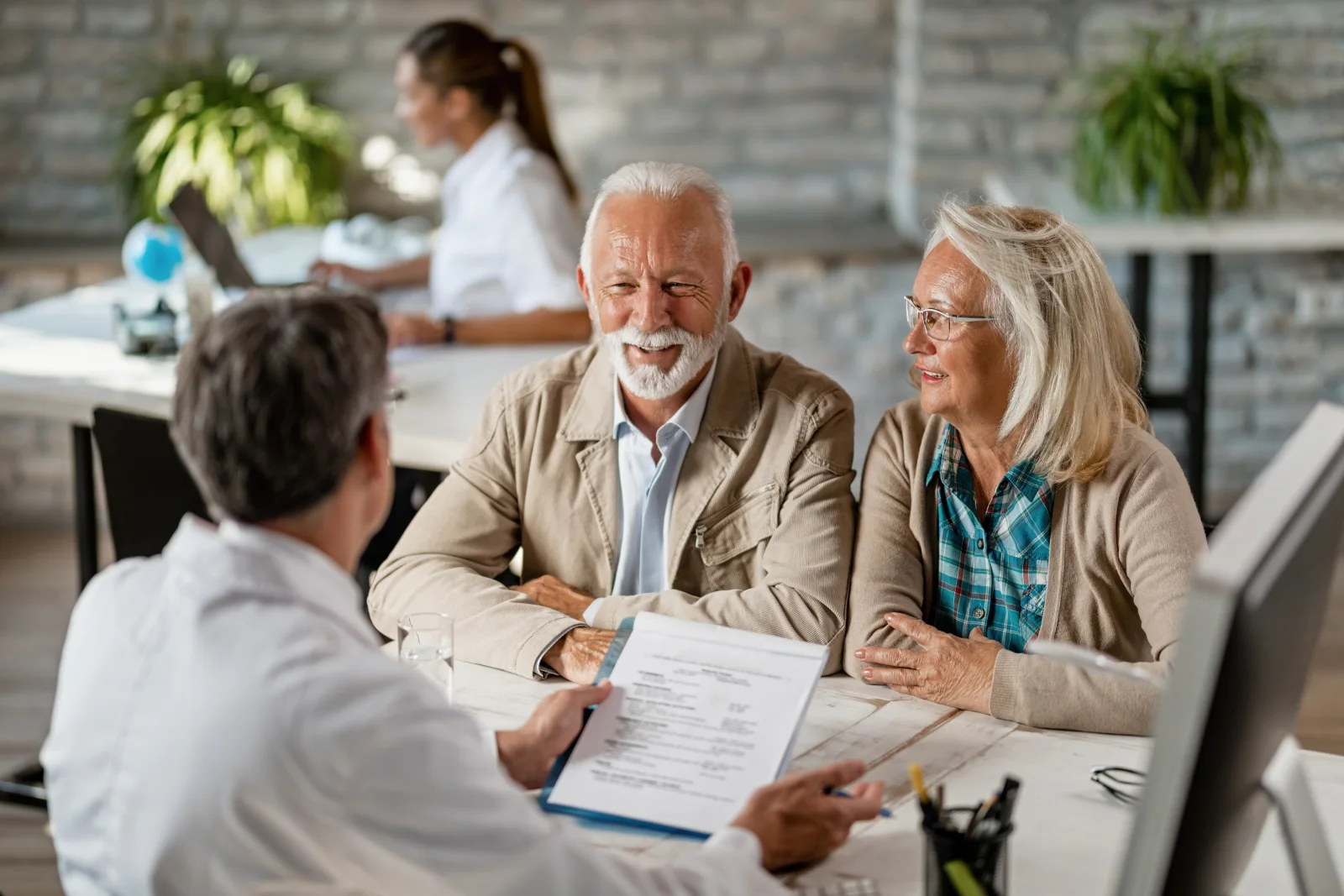 Un couple senior échange avec un professionnel de santé autour de documents présentant leurs garanties