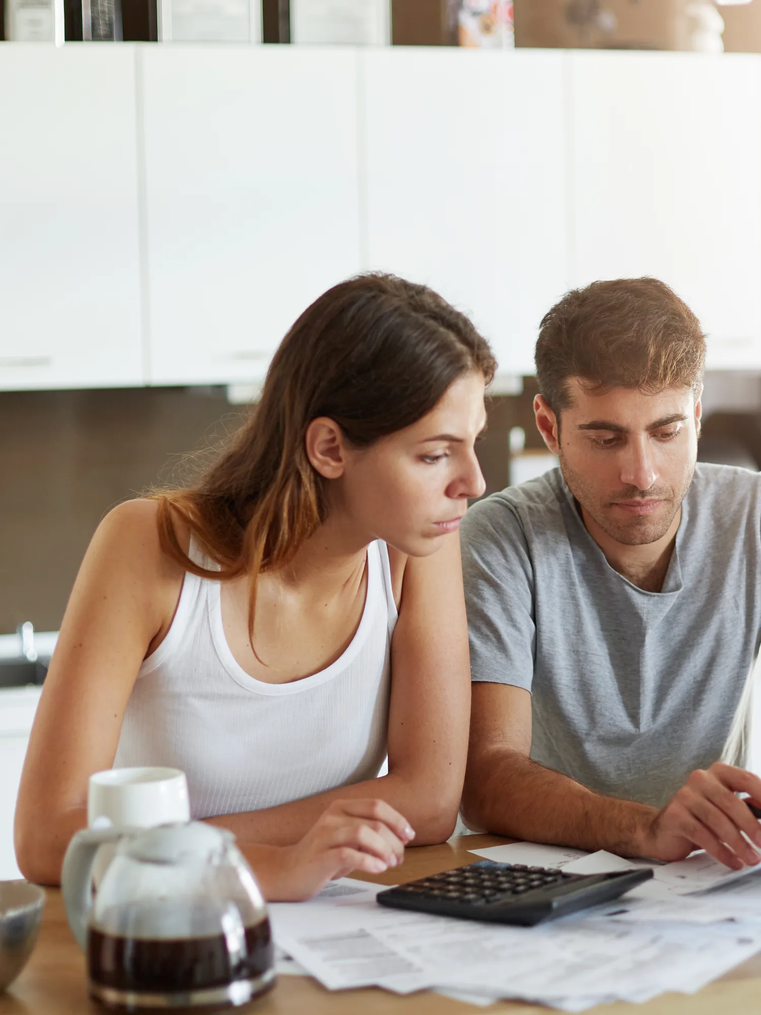 Un couple analyse des factures et utilise une calculatrice à la table de sa cuisine pour organiser son budget