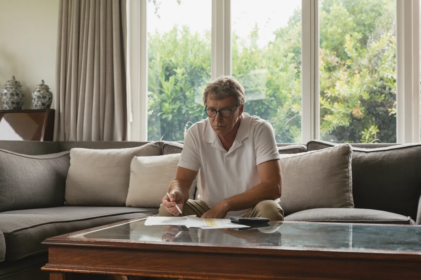 Un homme senior classe et annote des documents à la table basse de son salon lumineux