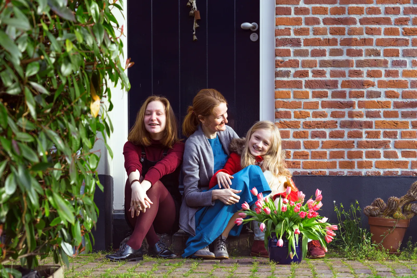 Une mère et ses deux filles discutent sur le perron fleuri de leur maison en briques