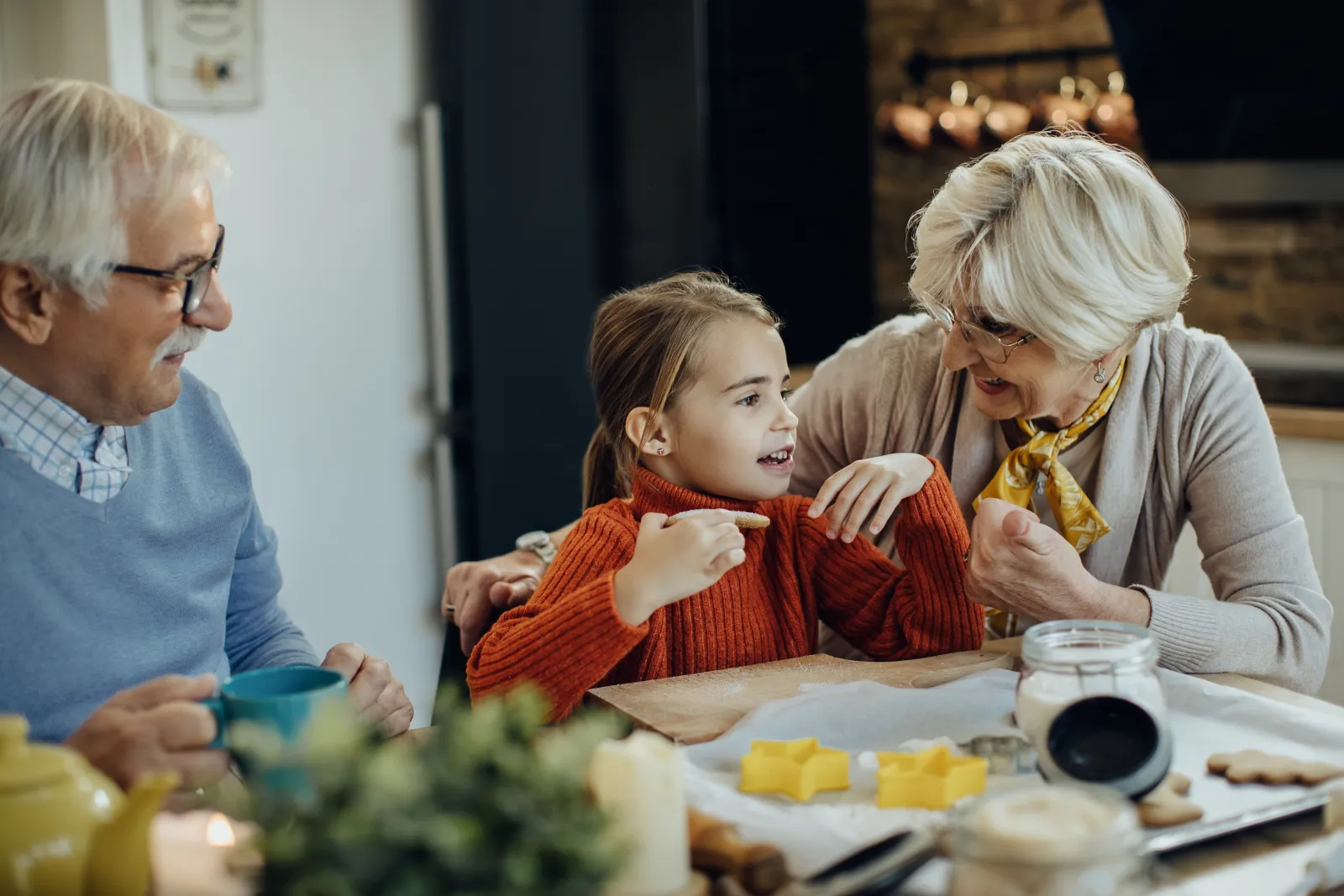Une enfant partage un moment en cuisine avec ses grands-parents autour d’une table baignée de lumière