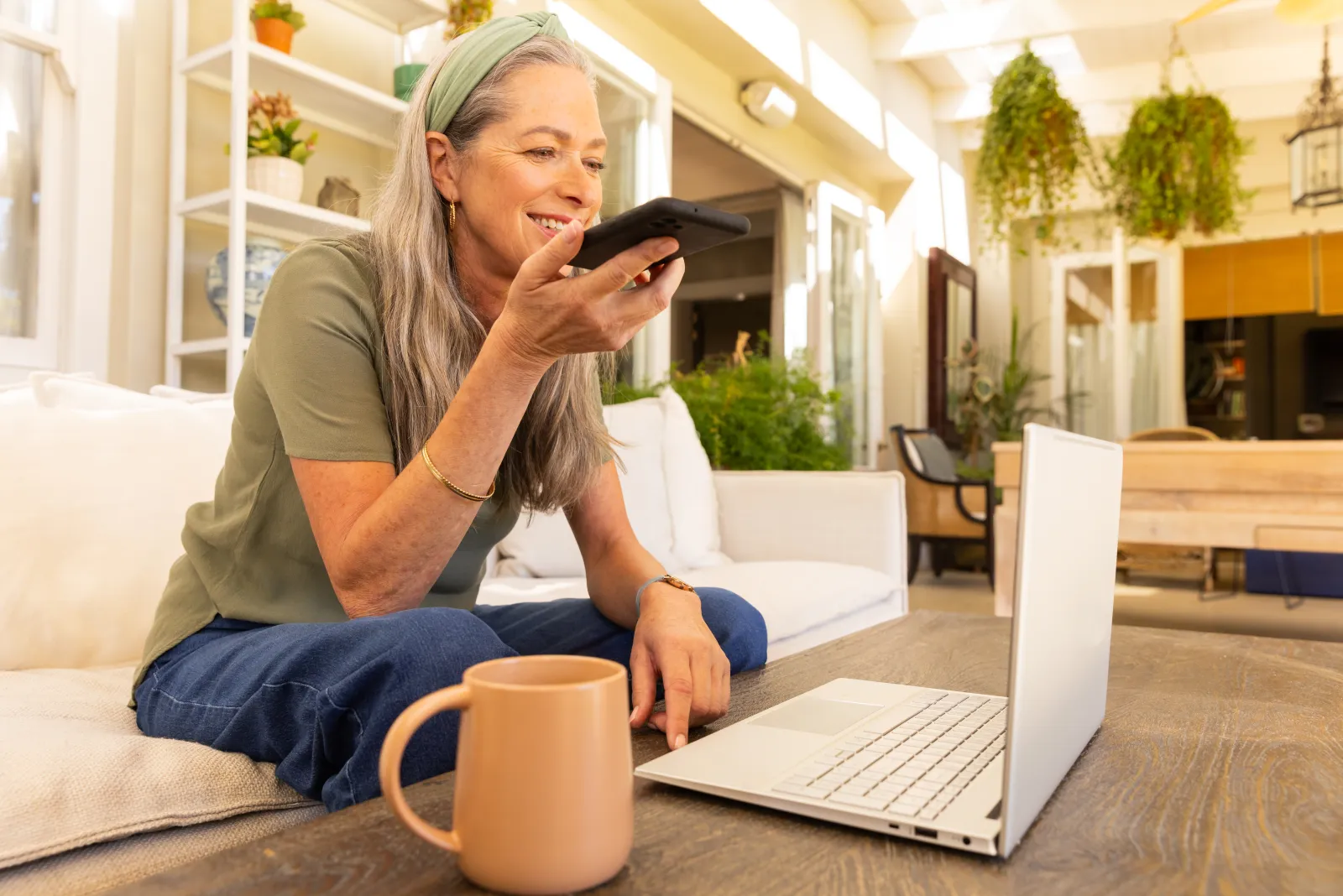 Une femme consulte son téléphone près de son ordinateur portable sur une terrasse lumineuse
